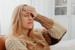 Vermoeide vrouw met blond haar op de bank met een gebreide trui 