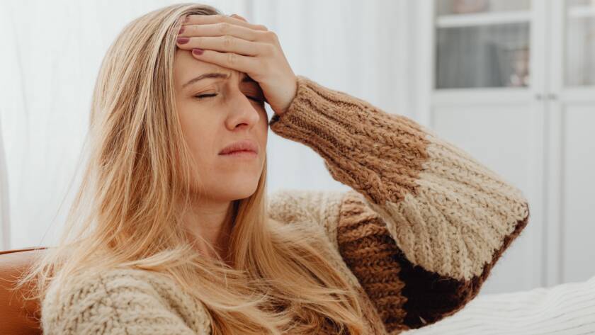 Vermoeide vrouw met blond haar op de bank met een gebreide trui